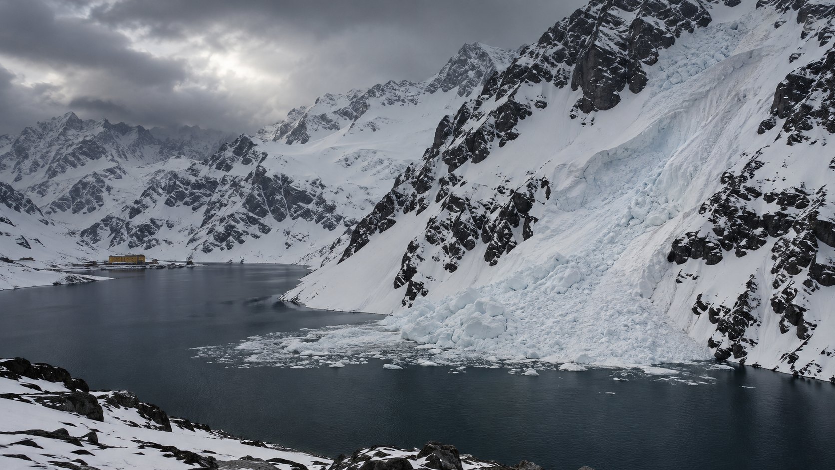 Ilustración editorial generada con IA: la Laguna del Inca, en la cordillera de los Andes chilena, rodeada de laderas con nieve profunda y una lengua de avalancha que baja por la montaña y entra en el agua oscura, bajo un cielo de tormenta, con el edificio amarillo del Hotel Portillo a lo lejos; composición conceptual, no es una fotografía de la avalancha.
