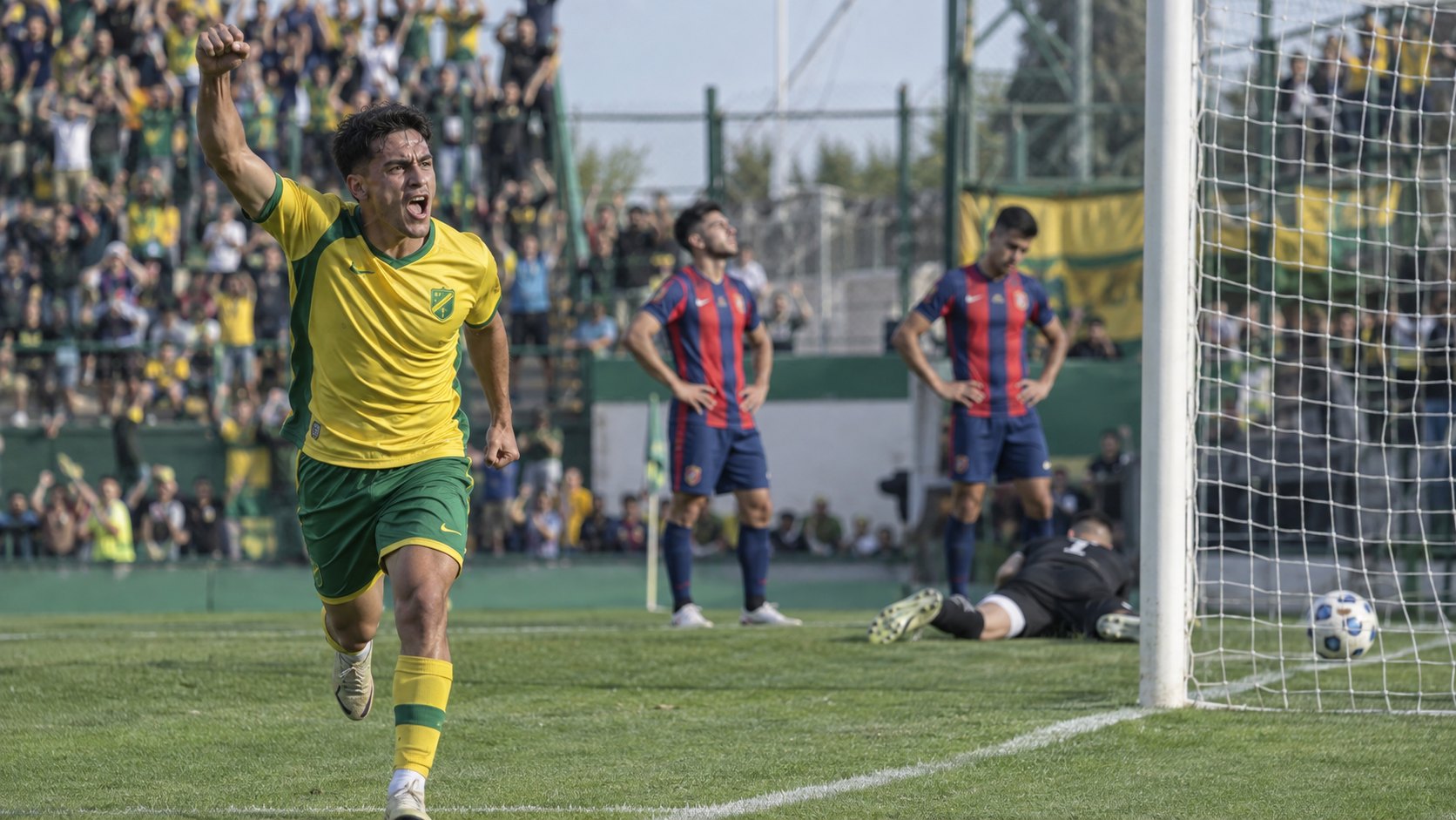 Ilustración editorial generada con IA: de día, un futbolista con la camiseta amarilla y verde de Defensa y Justicia festeja un gol con el puño en alto mientras, al fondo, dos jugadores con camiseta azulgrana se lamentan y el arquero queda en el piso junto a la pelota en la red; no es una fotografía del partido ni representa a jugadores reales.