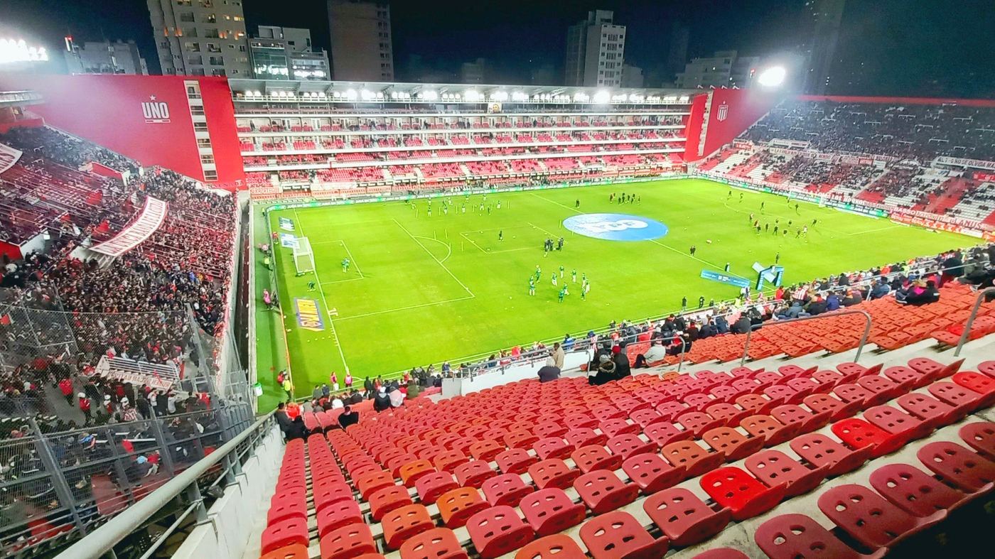 Vista nocturna del Estadio UNO (Jorge Luis Hirschi) de Estudiantes de La Plata colmado de público, con el sector UNO y la cancha iluminada antes de un partido