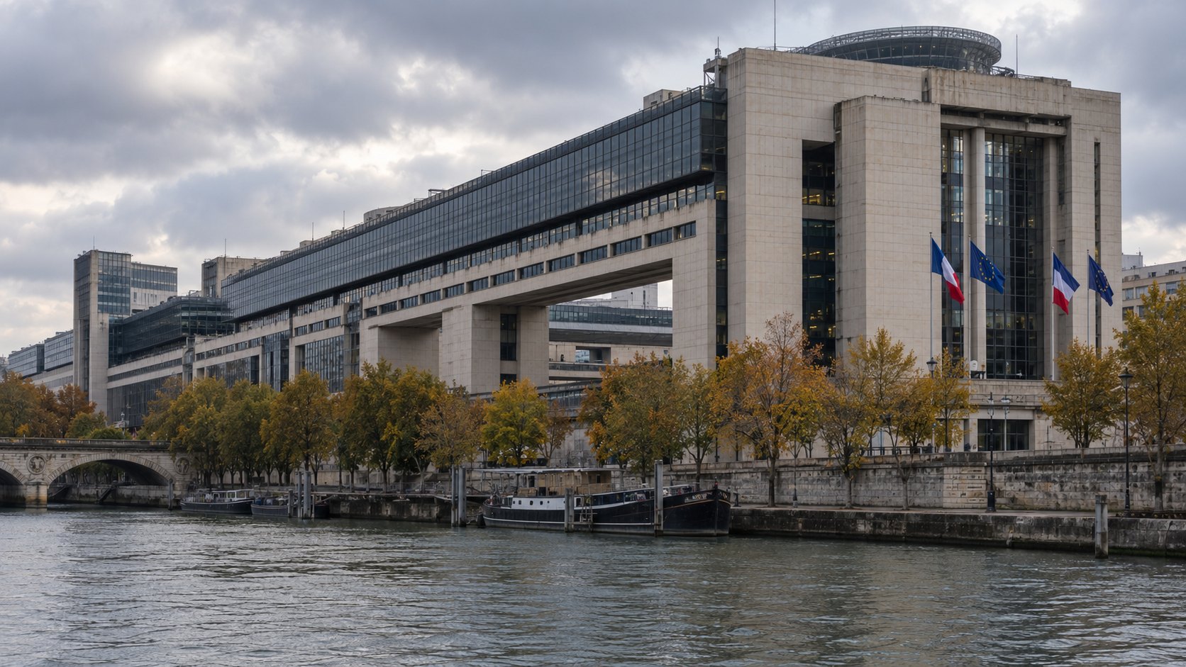Ilustración editorial generada con IA: el edificio del Ministerio de Economía y Finanzas de Francia en Bercy, París, que avanza sobre el Sena, con banderas de Francia y de la Unión Europea en la fachada, árboles otoñales y el río en primer plano bajo un cielo nublado; composición conceptual, no es una fotografía tomada el día del hecho.