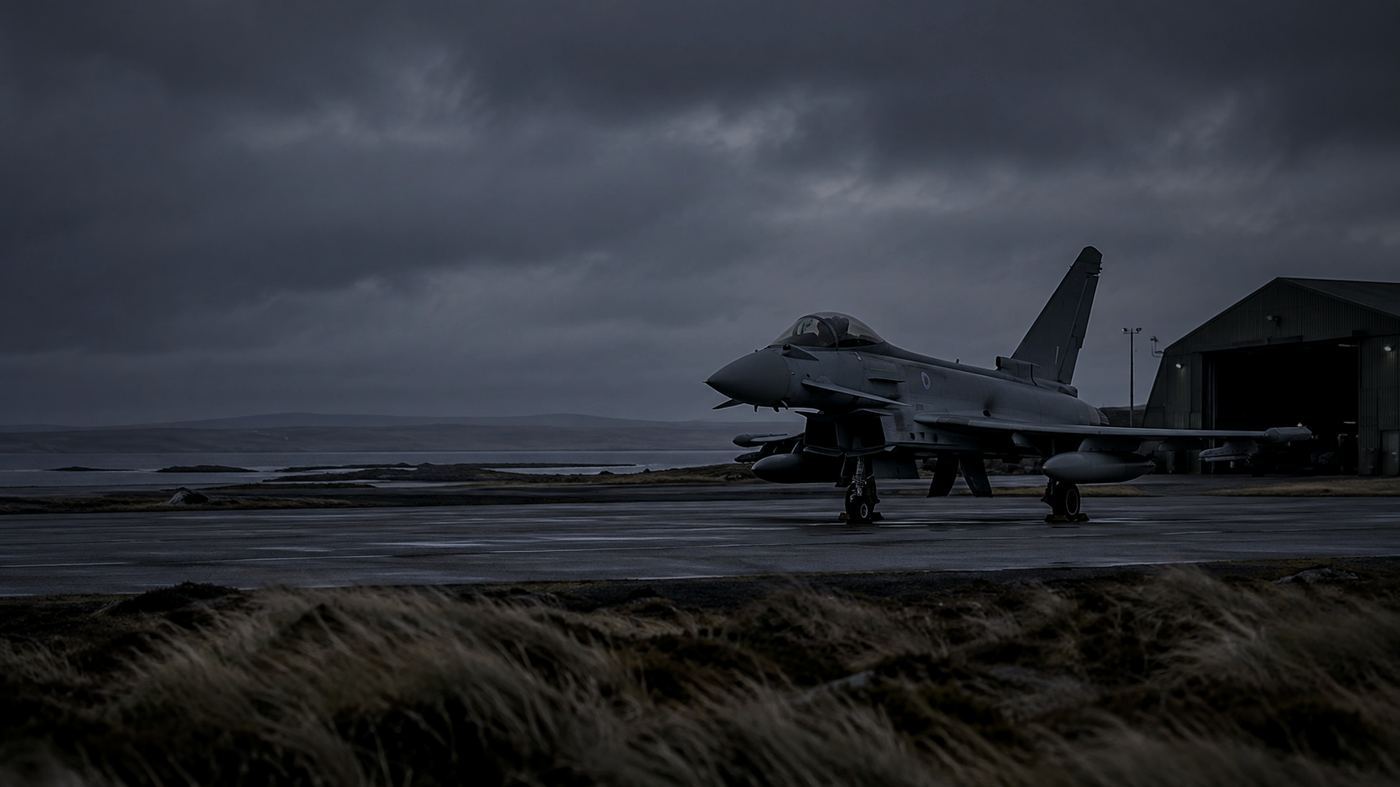 Avión de combate Eurofighter Typhoon estacionado en una base militar aislada, bajo un cielo gris ventoso