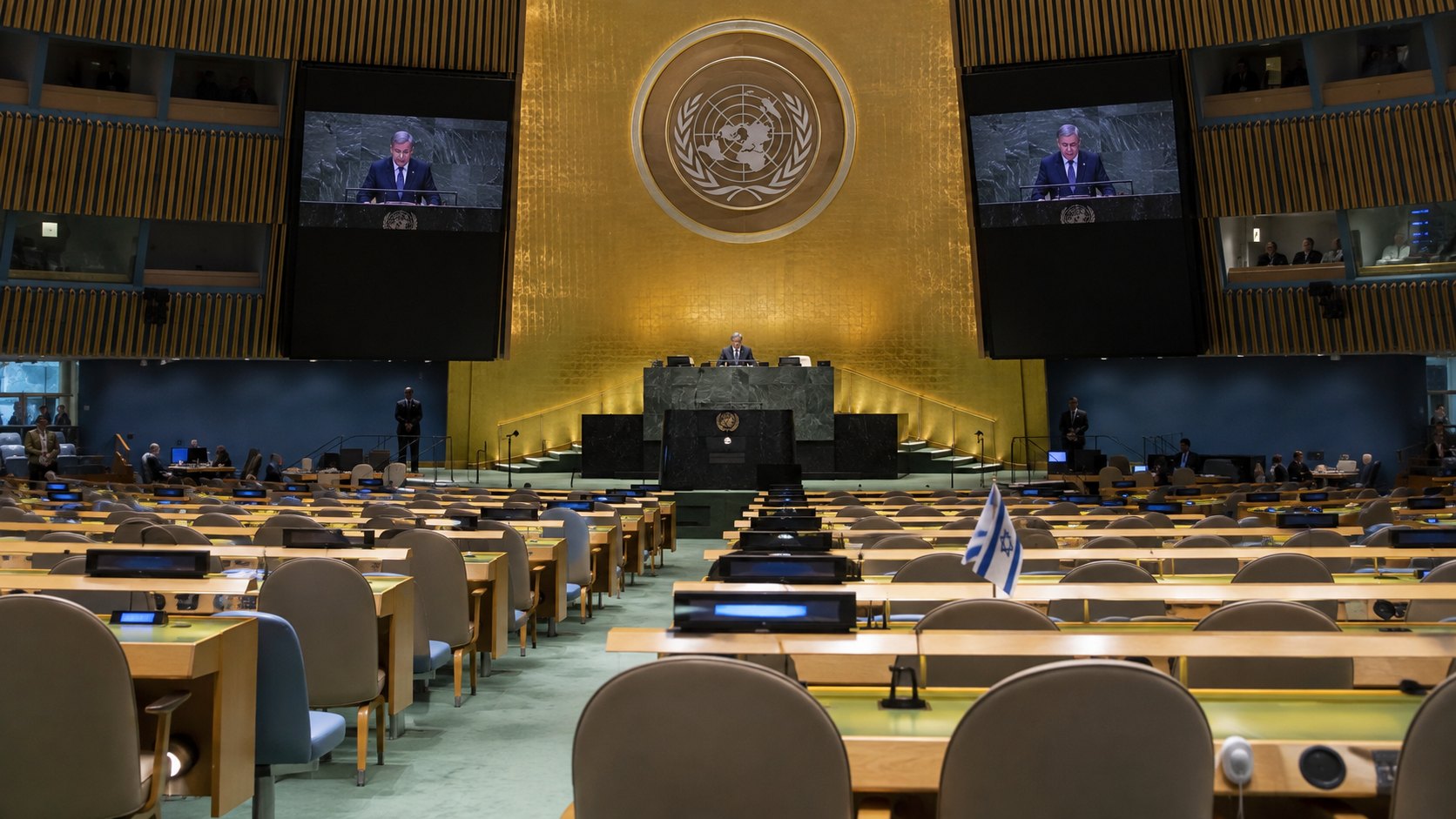 Ilustración editorial generada con IA: el salón de la Asamblea General de la ONU visto desde el fondo, con filas de bancas vacías y una pequeña bandera de Israel sobre un pupitre; no es una fotografía del discurso de Netanyahu.