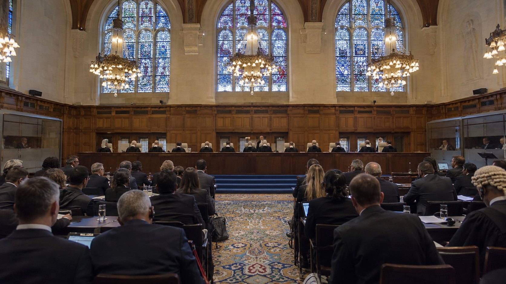 Ilustración editorial generada con IA: la Gran Sala de Justicia del Palacio de la Paz, en La Haya, con sus vitrales y jueces con toga negra en el estrado de la Corte Internacional de Justicia; composición conceptual, no es una fotografía de una audiencia real ni retrata a Navi Pillay.