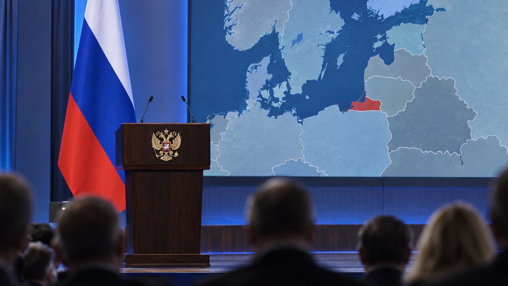 Ilustración editorial generada con IA: un atril con el escudo del águila bicéfala de Rusia y dos micrófonos sobre un escenario, junto a una bandera rusa y una pantalla con un mapa del mar Báltico que resalta en rojo el enclave de Kaliningrado, ante un público de espaldas; composición conceptual, no es una fotografía del foro Valdai.