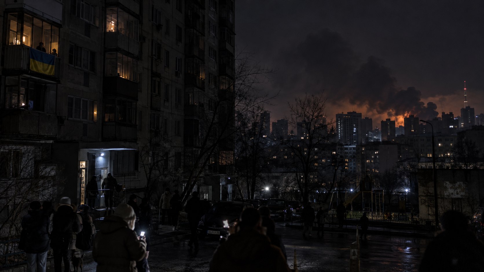 Ilustración editorial generada con IA: un barrio de edificios de departamentos de Kiev durante un apagón nocturno, con ventanas a oscuras, una bandera de Ucrania en un balcón, vecinos en la calle con linternas y humo iluminado en el horizonte; composición conceptual, no es una fotografía de los ataques del 16 de octubre.