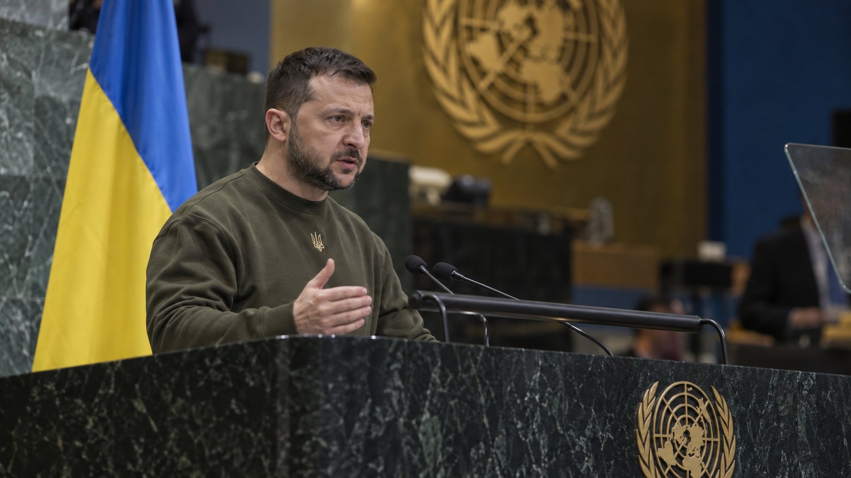 Ilustración editorial generada con IA: Volodímir Zelenski habla desde el estrado de la Asamblea General de las Naciones Unidas, junto a una bandera de Ucrania y con el emblema de la ONU al fondo; no es una fotografía del discurso.