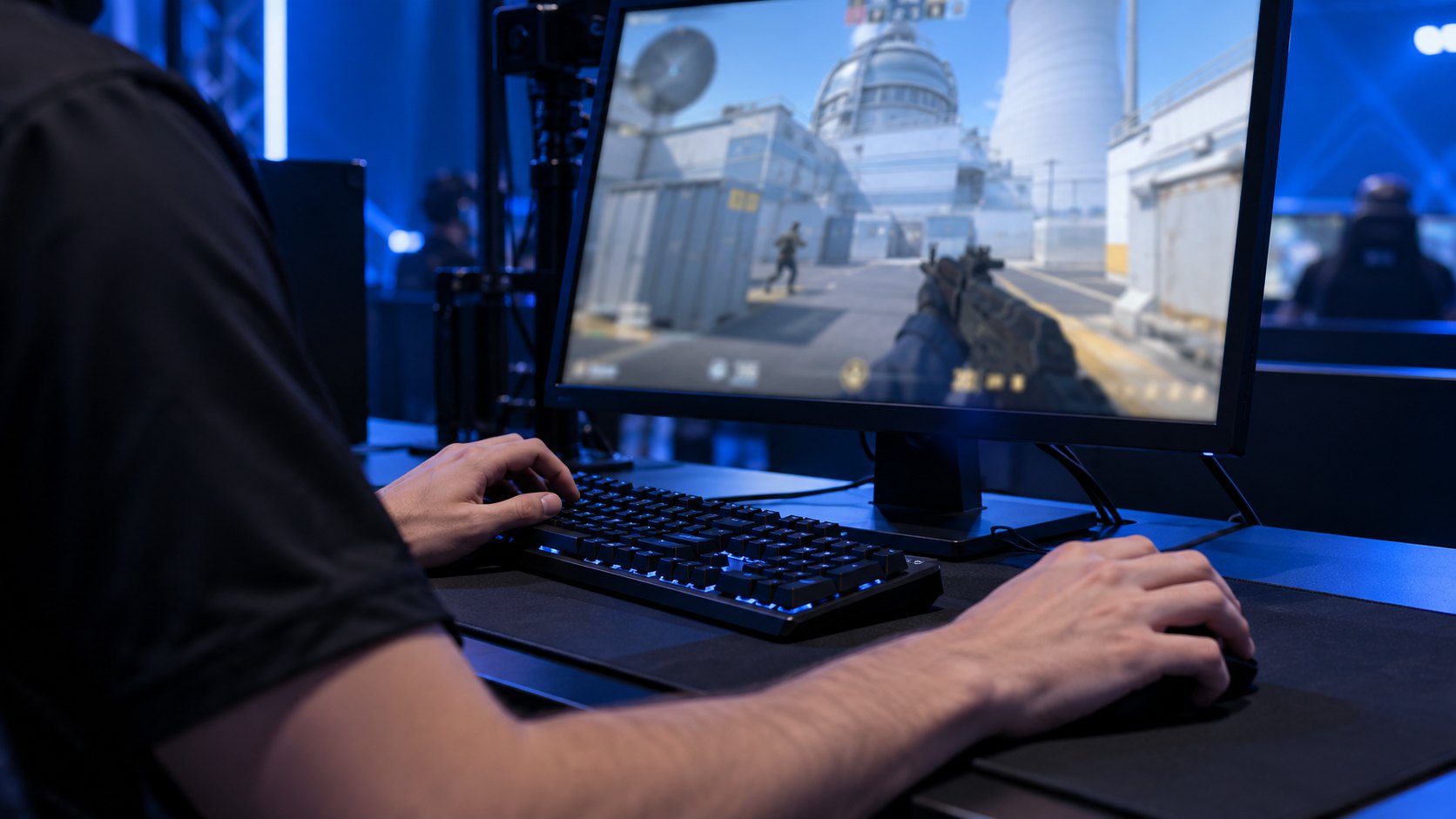 Ilustración editorial generada con IA: las manos de un jugador con camiseta negra sobre el teclado y el mouse, frente a un monitor con una partida de Counter-Strike 2 en el mapa Nuke, bajo luces azules de escenario; composición conceptual, no es una fotografía del partido.