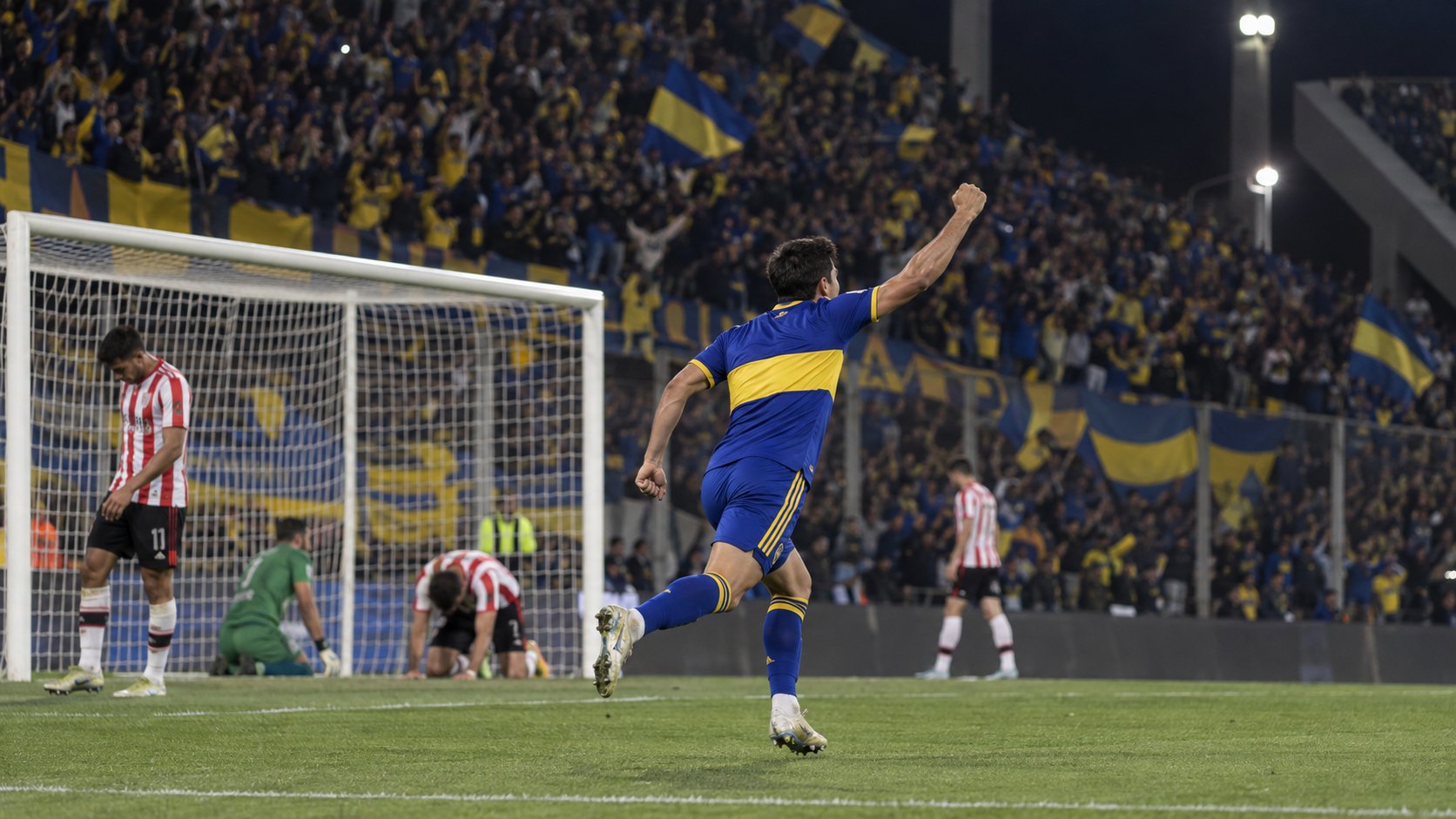 Ilustración editorial generada con IA: un futbolista con la camiseta azul y amarilla de Boca festeja el empate con el puño en alto frente a la tribuna visitante del Kempes; no es una fotografía del partido ni representa a jugadores reales.